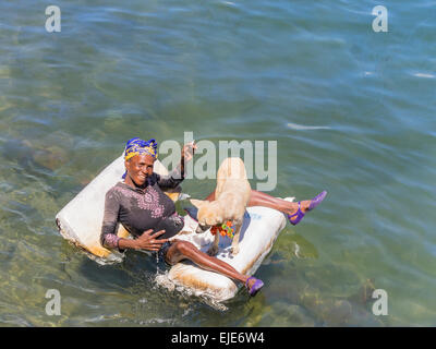 Une femme afro-mendiant allongé sur un radeau dans l'océan au large de Cayo Granma. Elle est accompagnée de son chien blanc. Banque D'Images