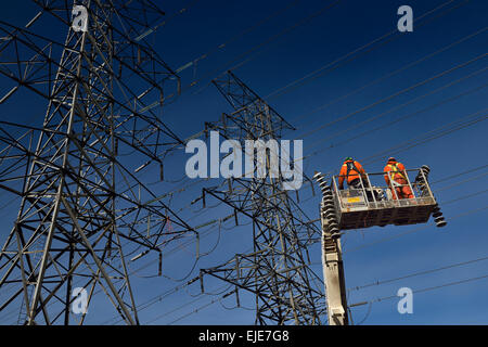 Les monteurs-hydro dans l'équipement de sécurité orange sur nacelle avec de vieux isolateurs de suspension de la ligne d'alimentation d'électricité haute tension Toronto tours on blue sky Banque D'Images