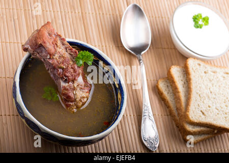 Soupe de légumes avec de la viande fumée, pain, crème et cuillère en argent sur nappe en bois Banque D'Images