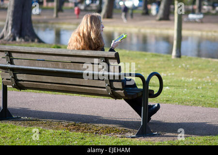 Les jeunes femmes checking mobile phone assis sur un banc sur le quai à Bedford, Bedfordshire, Angleterre Banque D'Images