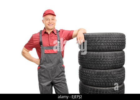 Homme mécanicien dans un chandail rouge et gris jumpsuit appuyée sur une pile de pneus isolé sur fond blanc Banque D'Images