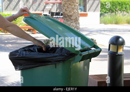 Une femme de jeter les ordures dans une grande poubelle verte dans un parc ou à l'extérieur salon symbolisant le recyclage dans les lieux publics Banque D'Images