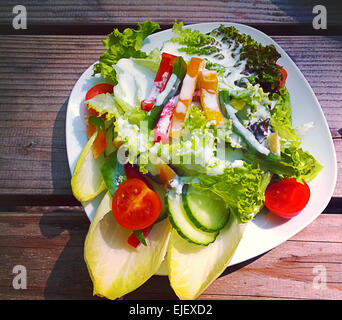 Salade mixte avec l'endive, tomates,poivrons,surmonté d'endives vinaigrette sur un banc en bois rustique. Banque D'Images