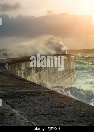 De grosses vagues sur la jetée de concassage de pierre courbe, sur un temps orageux avec des coucher de soleil, grande marée, Saint Malo, France. Banque D'Images