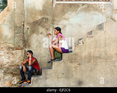 Deux personnes afro-cubaine, un homme et une femme, tous deux dans la vingtaine, installez-vous sur un escalier en béton par le côté d'une maison. Banque D'Images