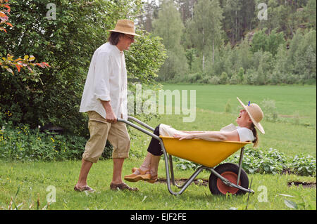 Hauts homme porte a senior woman dans une brouette à l'extérieur près d'un potager. Ils riaient et s'amusant. Banque D'Images
