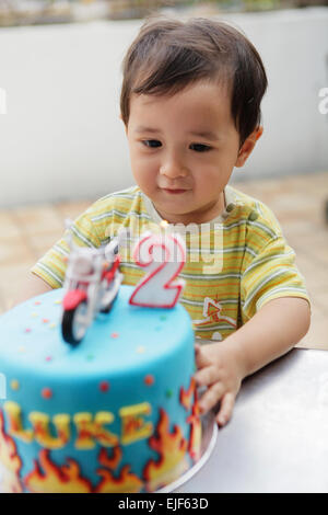Bébé garçon en tournant deux ans, soufflant la bougie sur son gâteau d'anniversaire Banque D'Images