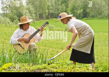 Les cadres supérieurs l'homme et la femme dans un potager. La femme est attentivement le sol. L'homme joue d'une guitare Banque D'Images