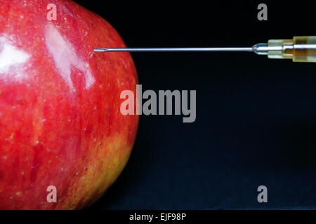 Aiguille hypodermique injecte une pomme rouge avec un liquide brun Banque D'Images