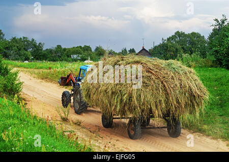 Paysage rural - tracteur passe sur chemin de sable avec remorque chargée de foin. Banque D'Images