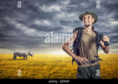 Homme avec des jumelles et rhino derrière dans les prairies au coucher du soleil Ciel couvert Banque D'Images