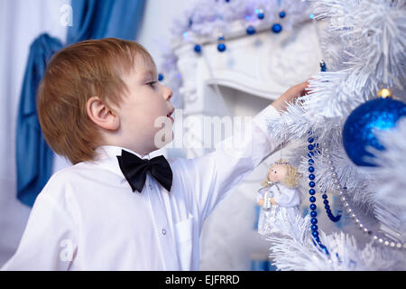 Petit garçon dans une chemise blanche et noeud papillon décore un arbre de Noël Banque D'Images