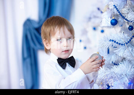 Petit garçon dans une chemise blanche et noeud papillon décore un arbre de Noël Banque D'Images