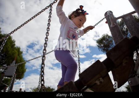 Belle petite fille escalade un petit pont en bois sur l'aire de jeux Banque D'Images