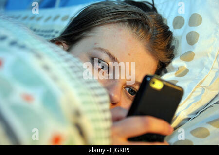 Teenage girl utilise son téléphone portable la nuit au lit. Banque D'Images