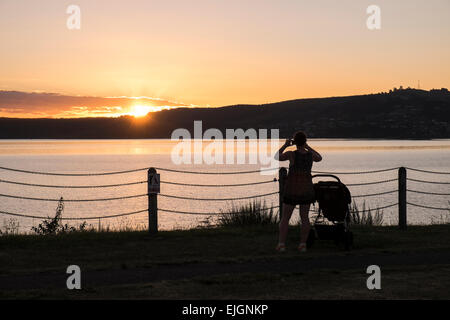 Femme de prendre une photo du coucher de soleil le long de la promenade au bord du lac au crépuscule à Taupo, Nouvelle-Zélande. Banque D'Images