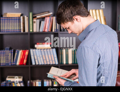 Close up le jeune homme à manches longues Shirt lire un livre à la bibliothèque au sérieux. Banque D'Images