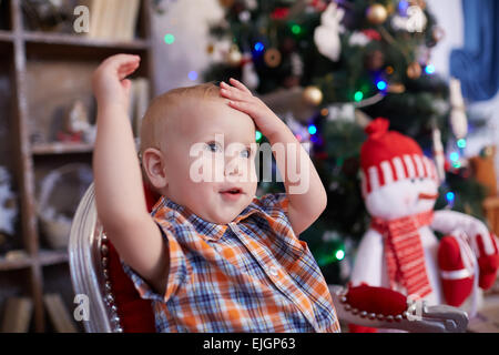 Enfant actif, enjoué est assis sur une chaise près de l'arbre de Noël Banque D'Images