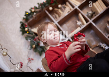 Garçon de cinq ans dans l'attente de la maison de vacances, assis près de l'arbre de Noël, tenant un bouquet de fruits rouges Banque D'Images