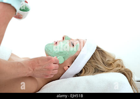 L'application de la beauté du visage thalasso vert masque avec un pinceau sur la joue d'une pose et à l'ambiance Belle blonde femme contre un Banque D'Images