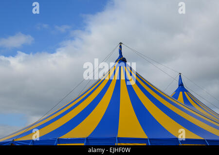 Toile rayée bleu et jaune du toit du cirque sous un ciel bleu avec des nuages blancs. Banque D'Images