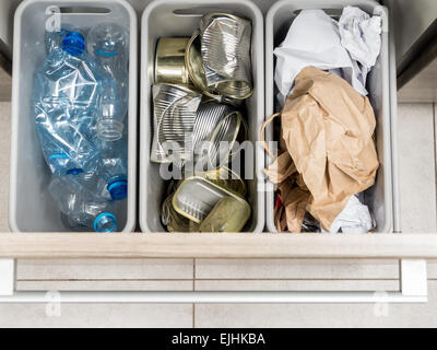 Trois poubelles en plastique dans l'armoire de cuisine avec séparation des déchets domestiques - Bouteilles PET, papier, boîtes métalliques en plongée des Banque D'Images