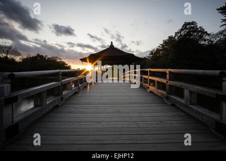 Coucher de soleil derrière un bâtiment japonais en bois au bout d'un pont au-dessus de l'étang Sagi Ike à Nara Park, Japon Banque D'Images