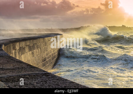 De grosses vagues sur la jetée de concassage de pierre courbe, sur un temps orageux avec des coucher de soleil, grande marée, Saint Malo, France. Banque D'Images