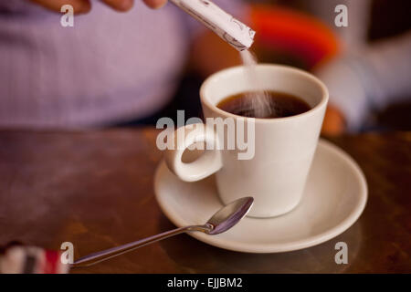 L'ajout de sucre à sa tasse en céramique blanche sur la terrasse du restaurant table. Selective focus Banque D'Images