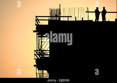 Les travailleurs de la construction sur un chantier de silhouettes au coucher du soleil Banque D'Images