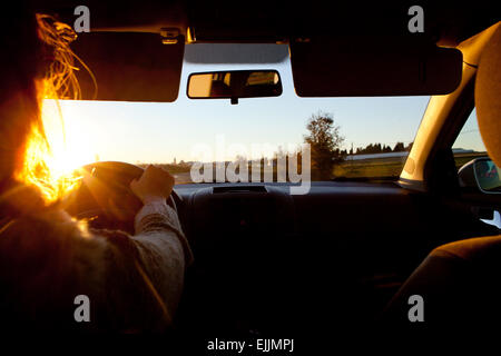 Une femme conduisant au coucher du soleil. Problèmes de vision dans ce jour heure Banque D'Images