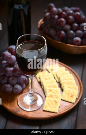 Verre de vin rouge avec du raisin red globe, craquelins et une bouteille de vin, photographié sur en bois avec éclairage naturel Banque D'Images
