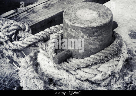 Ancienne borne d'amarrage rouillées avec cordes naval sur la jetée, photo en noir et blanc Banque D'Images