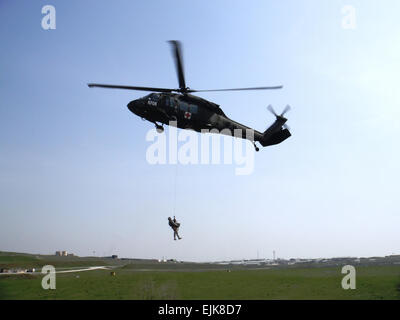 Le s.. Josh Rose, un maître-chien militaire et sous-officier responsable du Camp Bondsteel chenil, est hissé vers le ciel de plus de 50 pieds, avec son chien de travail militaire, bouclier, pour un vol stationnaire UH-60 Black Hawk à Camp Bondsteel, le Kosovo, le 2 avril. Les attelages de l'air en partenariat avec les équipes de l'évacuation médicale de la Garde nationale de la Louisiane 2e bataillon du 135e Régiment d'aviation, pour s'entraîner sur des procédures nécessaires à l'évacuation des blessés un chien provenant d'un champ de bataille de blessures. Le capitaine Nathan Carlton, 61e Bataillon Médical multifonctionnel Banque D'Images