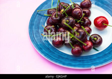 Cerises biologiques sur une plaque sur fond rose Banque D'Images