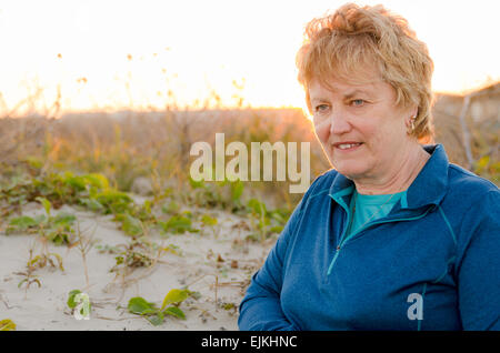 Hauts Femme Age 60-65 debout avec le soleil à son retour dans les dunes de sable près de la plage à détendu et heureux Banque D'Images