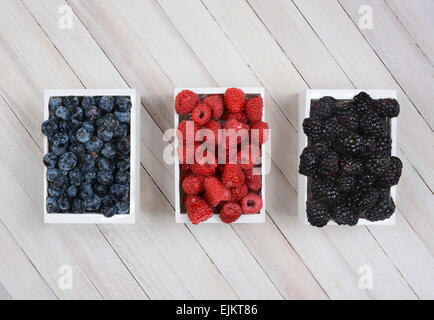 Trois mini-caisses en bois de petits fruits sur une surface en bois rustique. Les Bleuets Framboises et mûres dans les petites cases blanches Banque D'Images