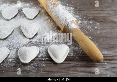 Les boulettes en forme de cœur, de farine et de rouleau à pâtisserie sur fond de bois. Ravioles de cuisson. Profondeur de champ. Banque D'Images