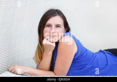 Photo de jolie jeune femme aux cheveux longs dans un tee-shirt bleu. Portrait d'une jeune fille couchée et étaiement visage dans ses mains fermer Banque D'Images