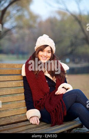 Jeune fille assise sur un banc dans un parc en hiver looking at camera Banque D'Images