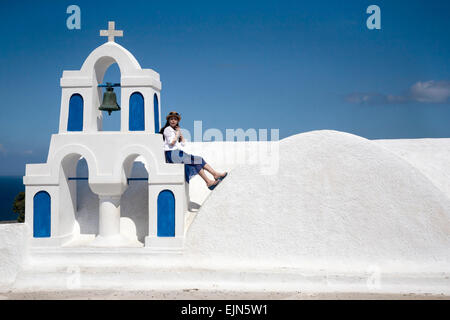 Fille assise à côté de cloches de l'Église orthodoxe grecque, Oia, Santorin (Théra), Grèce. Banque D'Images