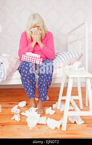 Pyjama rose avec femme triste et tissus sitting on bed blowing her nose Banque D'Images