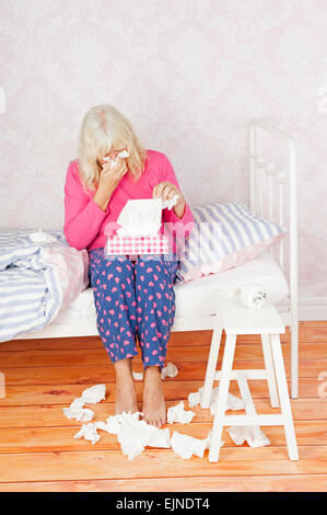 Pyjama rose avec des femmes et des tissus assis sur le lit en désespoir de Banque D'Images