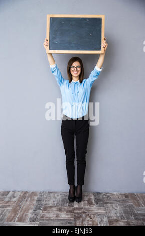 Portrait of a smiling businesswoman standing avec billboard. En chemise bleue et portant des lunettes. Looking at camera Banque D'Images