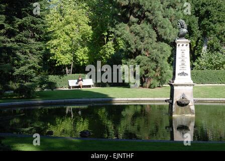 Femme assise sur un banc de parc se détendre et lire un livre à côté d'un lac, Buen Retiro Park, Madrid, Espagne Banque D'Images