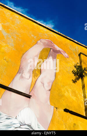 Graffiti dans la ville de Bristol de jambes pointant vers un ciel bleu sur un fond jaune/orange. Banque D'Images