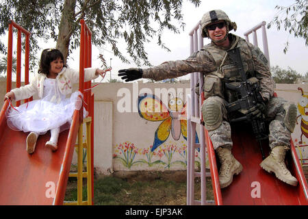 Le Sgt. Stephen Covell, originaire de Pacific Grove, en Californie, ainsi qu'une jeune fille iraquienne descendre une diapositive à l'aire de jeu pendant la réouverture de l'Al-Moutasam La Maternelle 3 mars dans le quartier de Rusafa de l'est de Bagdad. Covell est un infirmier affectés au siège des troupes et de l'Administration centrale, 5e Escadron, 73e Régiment de cavalerie, 3e Brigade Combat Team, 82e Division aéroportée, Multi-National Division-Baghdad Banque D'Images