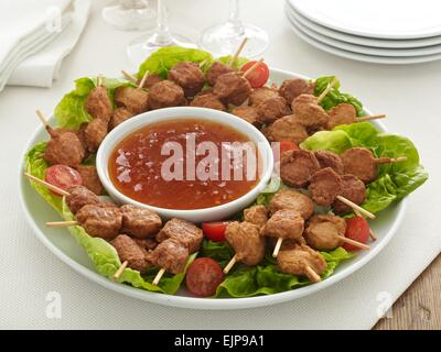 Plaque de buffet les morceaux de poulet sur des brochettes en bois avec une trempette au chili doux la laitue et les tomates Banque D'Images