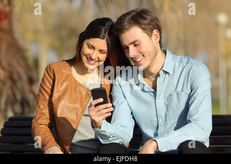 Heureux couple regardant un téléphone intelligent assis sur un banc dans un parc Banque D'Images