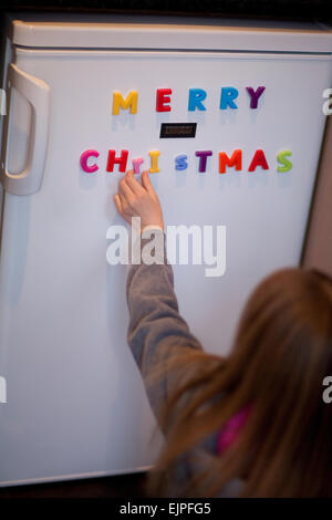 Jeune enfant collant magnétique coloré sur un réfrigérateur de lettres les mots 'merry Christmas'. Banque D'Images